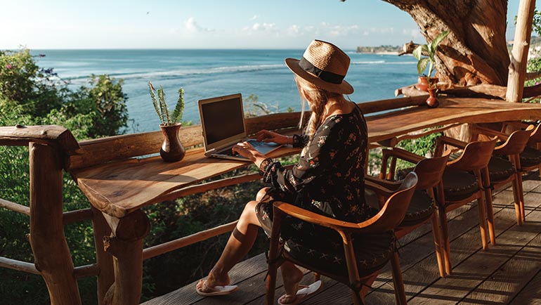 Freelance concept. Pretty young woman using laptop in cafe on tropical beach in outdoor cafe terrace with sea view. Work and travel